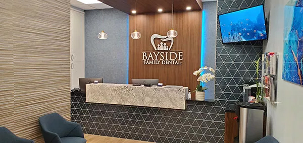 The image depicts an interior view of a dental office reception area with a modern design featuring a colorful wall, a reception desk, and a waiting area.
