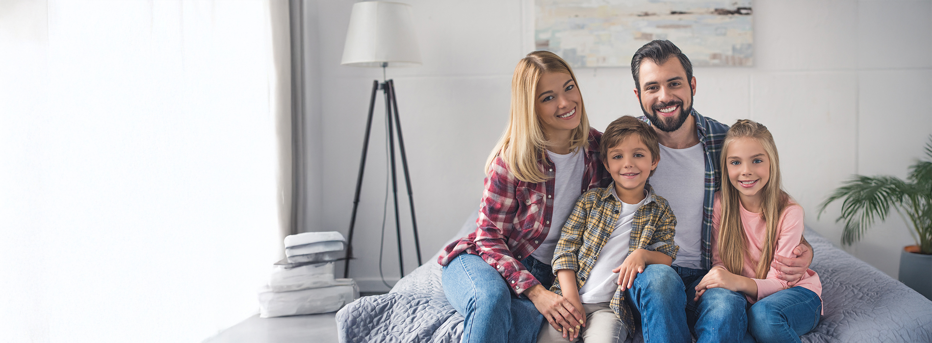 The image depicts a family of four, including two adults and two children, sitting together on a couch with a cozy home environment in the background.