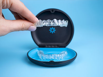 An open dental retainer case with a clear retainer inside, placed on a blue surface.